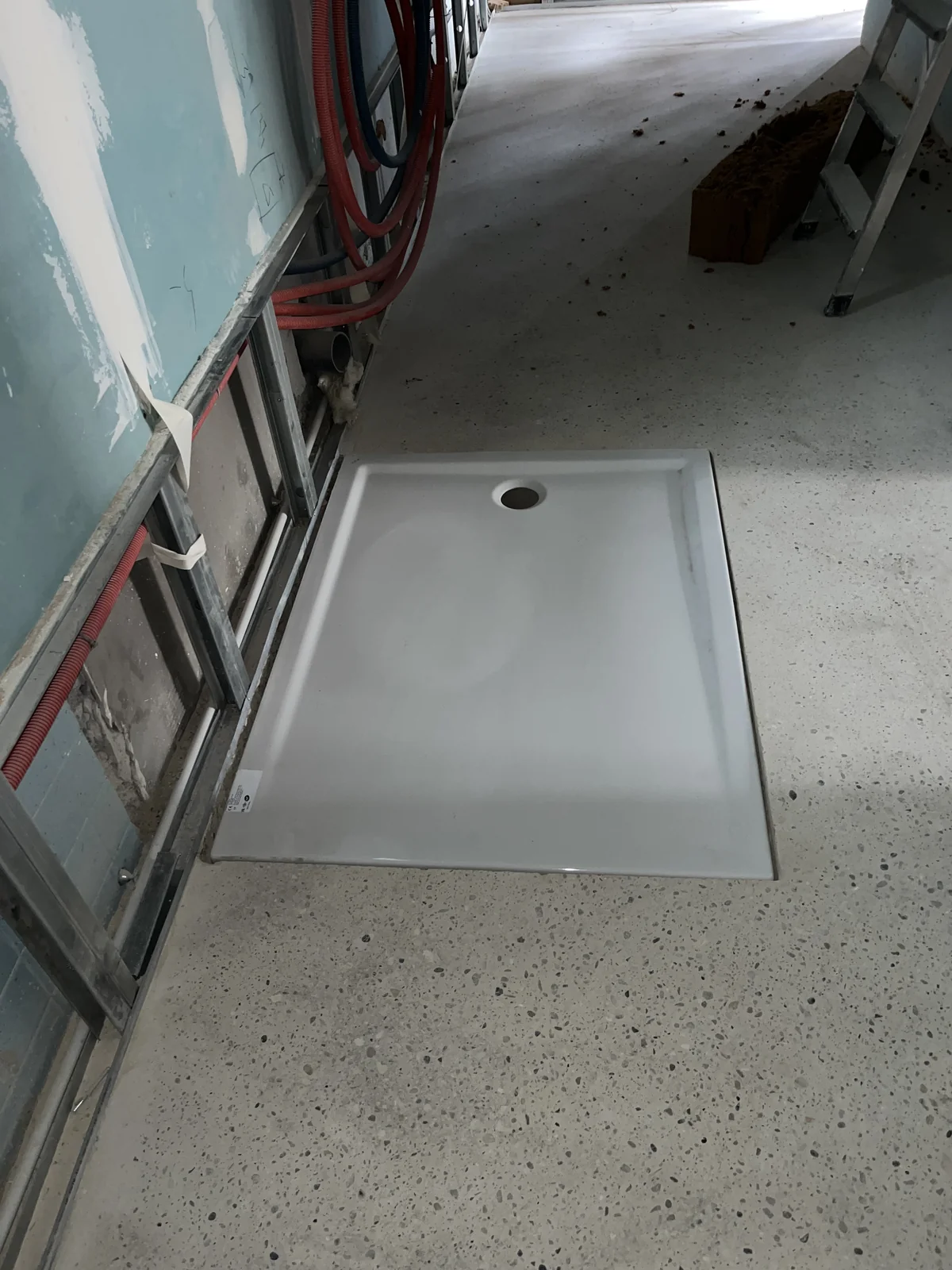Receveur de douche blanc et réseaux de plomberie visibles dans les cloisons en cours de travaux.